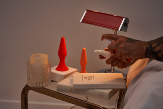 A man dripping Peach and Cream personal lubricant on a butt plug by his nightstand