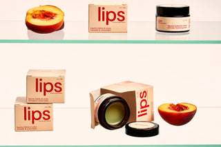 Peach and Cream vulva balm 'Lips' products with peach slices on a glass shelf
