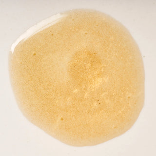 Close-up of Peach and Cream dry body oil 'Silk', a bronze and golden glitters liquid droplet on a white background