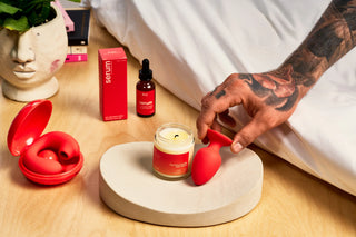 Person interacting with aPeach and Cream Uno plug, massage candle, Glow Vibrator and serum intimate gel on a wooden surface