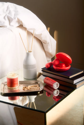 peach and cream vibrator lubricant and massage candle by a bed