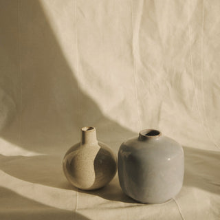 Two small ceramic vases in soft shadow on cream linen