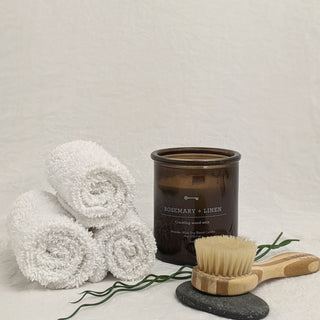 Rolled white towels, a candle and a bath brush