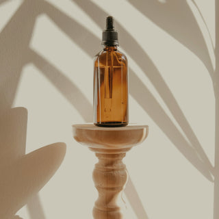 An amber glass oil bottle on a wooden stand in soft shadow