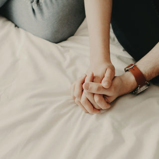 Two hands clasped on white bed sheets