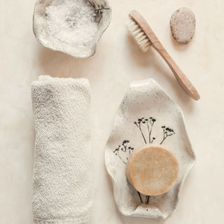 A rolled towel, soap and bath brush laid out on a light surface