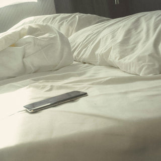 A phone lying on rumpled white bed sheets