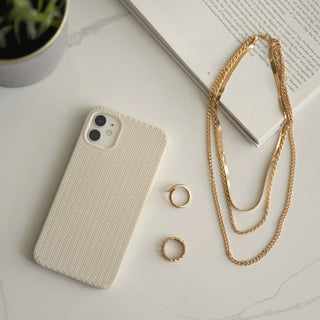 A cream phone beside gold rings and necklaces on a light surface