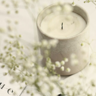 A lit white candle beside baby's breath flowers