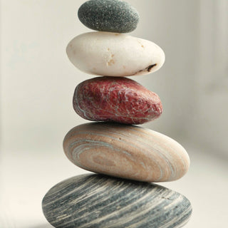 Smooth stacked pebbles, one of them red, on a light background