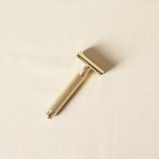 A gold safety razor on a cream background