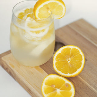 A glass of lemon water with lemon halves on a wooden board