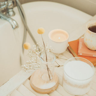 A bath tray with a candle, flowers and skincare in warm light
