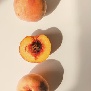 Ripe peaches, one halved, in warm sunlight on a cream background