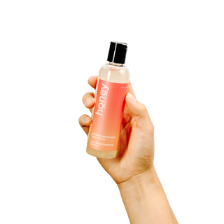 woman holding peach & cream honey natural personal lubricant bottle - lifestyle shot
