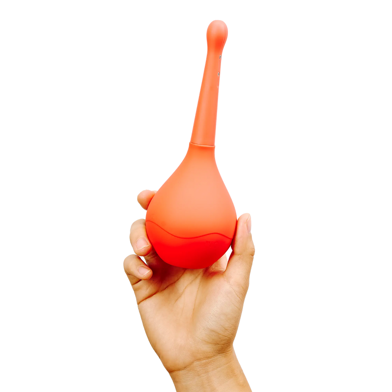 A hand holding a silicone enema bulb from peach and cream, named flush