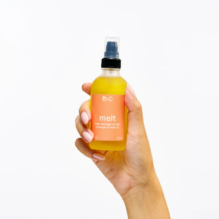 Hand holding a bottle of peach and cream 'melt' massage & bath oil against a white background
