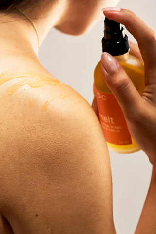 Person applying a Peach and Cream 'melt' massage oil to their shoulder against a neutral background