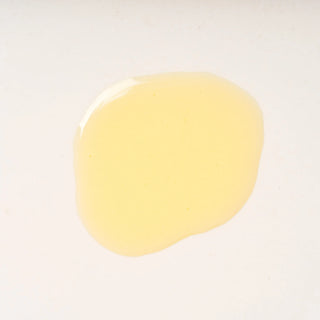 Close-up of Peach and Cream shaving primer 'Base', a yellowish liquid droplet on a white background
