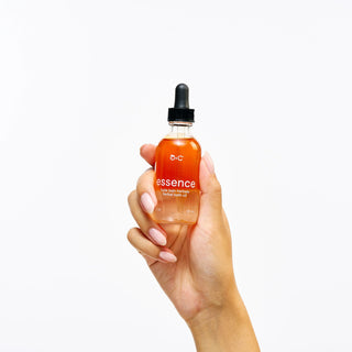 Hand holding a bottle of Peach and Cream botanical oil 'essence' with a white background