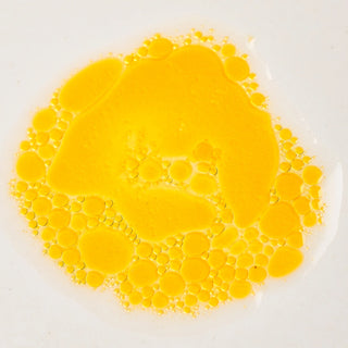 Close-up of Peach and Cream botanical oil 'Essence', a orange and transparent liquid droplet on a white background