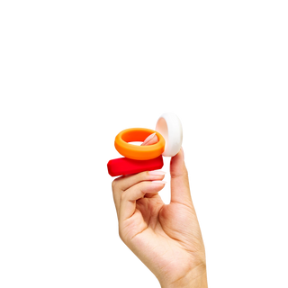 Hand holding Peach and Cream 'O' intimate silicone ring set, one red and one orange, one white