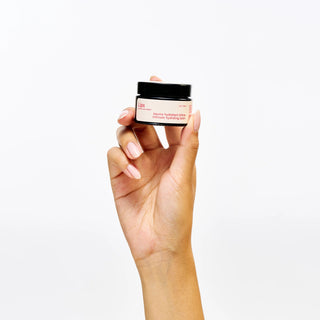 Hand holding a small jar of Peach and Cream 'lips' vulva balm against a white background