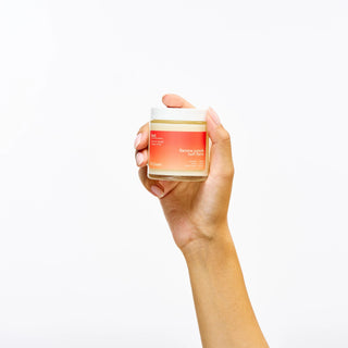 Hand holding a jar of Peach and Cream Twin Flame Massage candle against a white background