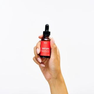 Hand holding a bottle of Peach and Cream 'serum' tonic intimate gel with a red label on a white background