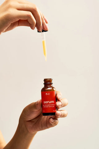 Hand holding Peach and Cream intimate gel 'serum' bottle with dropper against a plain background