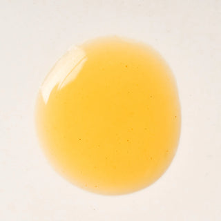 Close-up of Peach and Cream intimate gel 'Serum', a yellowish-orange liquid droplet on a white background