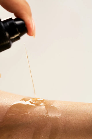 Hand applying a Peach and Cream dry body oil 'Silk' to a person's arm with a dropper bottle.