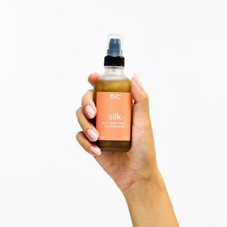 Hand holding a bottle of Peach and Cream 'silk' dry body oil against a white background