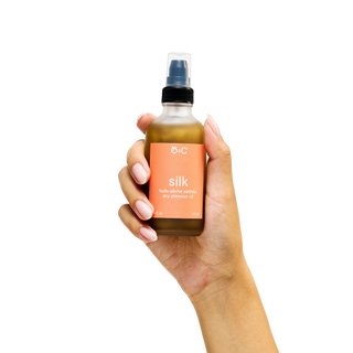Hand holding a bottle of Peach and Cream 'silk' dry body oil 