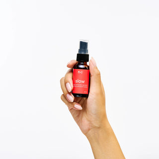 Hand holding a Peach and Cream calming sensation spray 'slow' against a white background