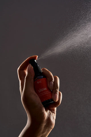 Hand holding a Peach and Cream spray bottle labeled 'slow' against a dark background