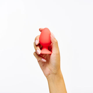 Hand holding a red Peach and Cream Uno Plug against a white background