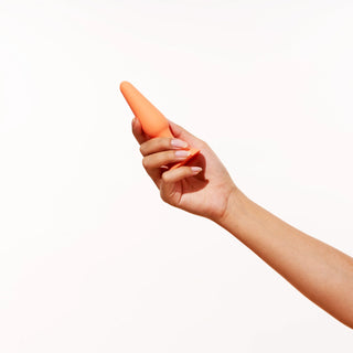Hand holding a Peach and Cream butt plug against a white background